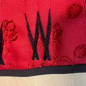 May include: Close-up of a red fabric with a black embroidered "W" and a repeating pattern of red circles. The fabric has a black trim.