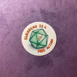 May include: A white round sticker with a green and orange dice and the text "Swearing is a Free Action".