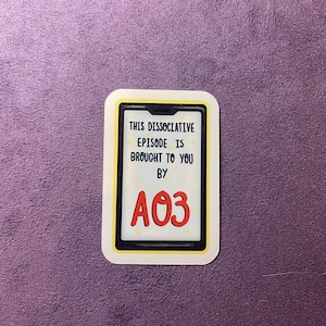 Op de afbeelding: Een witte sticker met een gele rand en een zwart telefoonscherm. Het scherm heeft witte sterren en rode tekst die "This Dissociative Episode is Brought to You by A03" luidt.