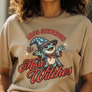 May include: A tan t-shirt with a graphic of a frog wearing a wizard hat and the text "Less Snitchers More Witches".