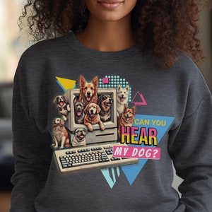 May include: Dark gray sweatshirt featuring a retro design with various dog breeds inside a vintage computer monitor. The text "CAN YOU HEAR MY DOG?" is displayed in a colorful, 80s-inspired font, with geometric shapes.