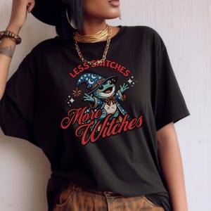 May include: Black t-shirt with a cartoon frog wearing a wizard hat and the text "Less Snitches More Witches".