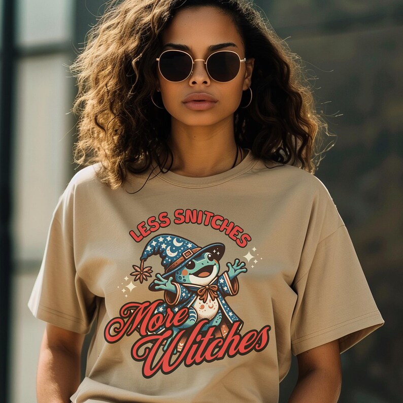 May include: A tan t-shirt with a graphic of a frog wearing a wizard hat and the text "Less Snitchers More Witches".