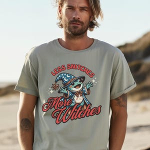 May include: A light green t-shirt with a cartoon frog wearing a wizard hat and robe. The text on the shirt reads "Less Snitchers More Witches".