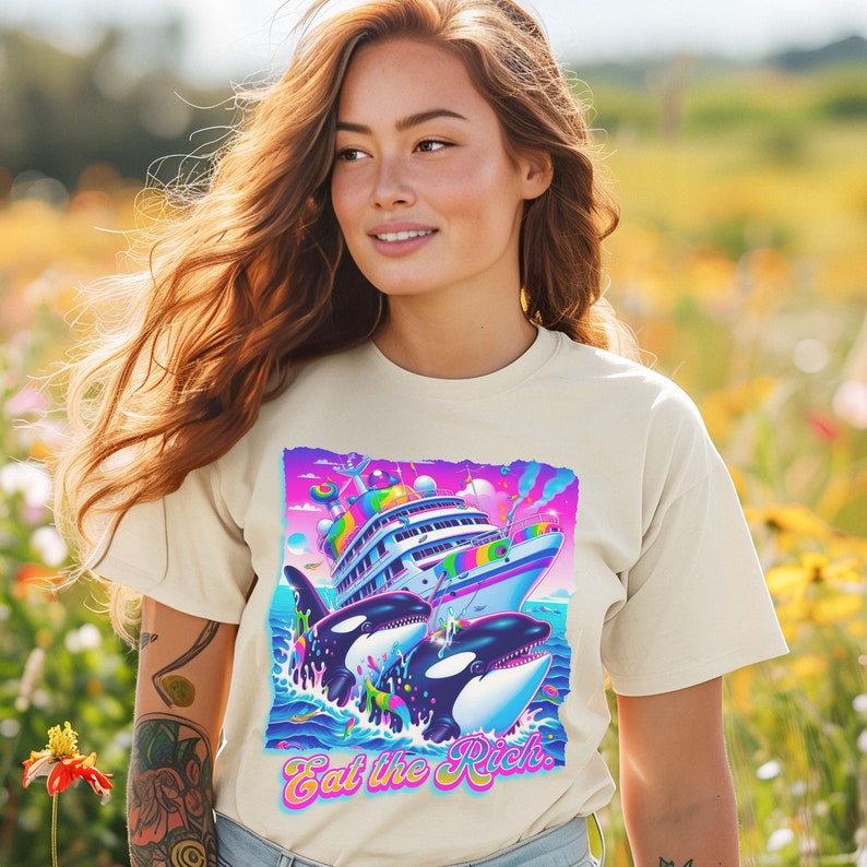May include: A white t-shirt with a graphic print of two orcas swimming towards a large yacht. The yacht is decorated with rainbow colors and has a pink and blue sky in the background. The text "Eat the Rich." is printed in pink and blue letters below the orcas.