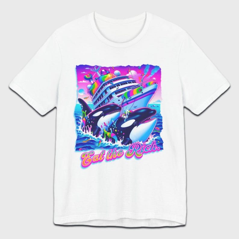 May include: White t-shirt with a graphic print of two killer whales jumping out of the water and attacking a large cruise ship. The graphic is in a rainbow color scheme and the text "Eat the Rich" is printed below the whales.
