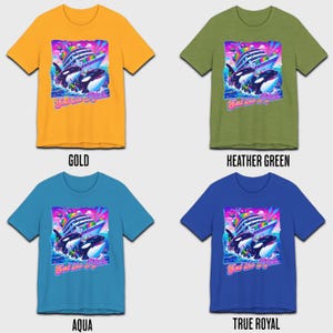 May include: Four t-shirts in different colors featuring a graphic of two orcas jumping out of the water with a cruise ship in the background. The graphic is in a retro 90s style with bright colors and a rainbow. The text "Eat the Rich" is printed below the graphic.