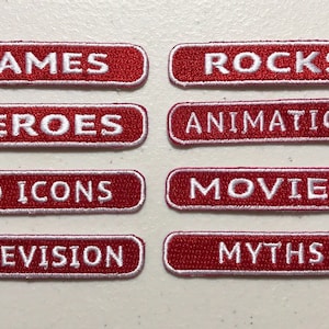 May include: Eight red rectangular patches with white embroidered text. The text reads: "GAMES", "ROCKS", "HEROES", "ANIMATION", "AD ICONS", "MOVIES", "TELEVISION", and "MYTHS".
