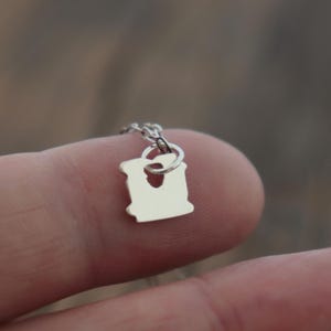 May include: A small, silver-coloured metal charm shaped like a slice of bread, featuring a cutout hole at the top. The charm is attached to a thin, delicate silver-coloured metal chain link, creating a miniature pendant design with a smooth, reflective surface.