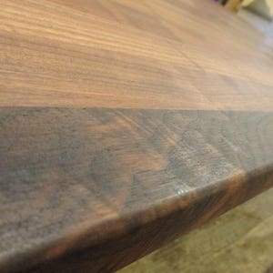 May include: Close-up of a dark brown wooden countertop with a lighter brown edge. The wood grain is visible and the surface is smooth.