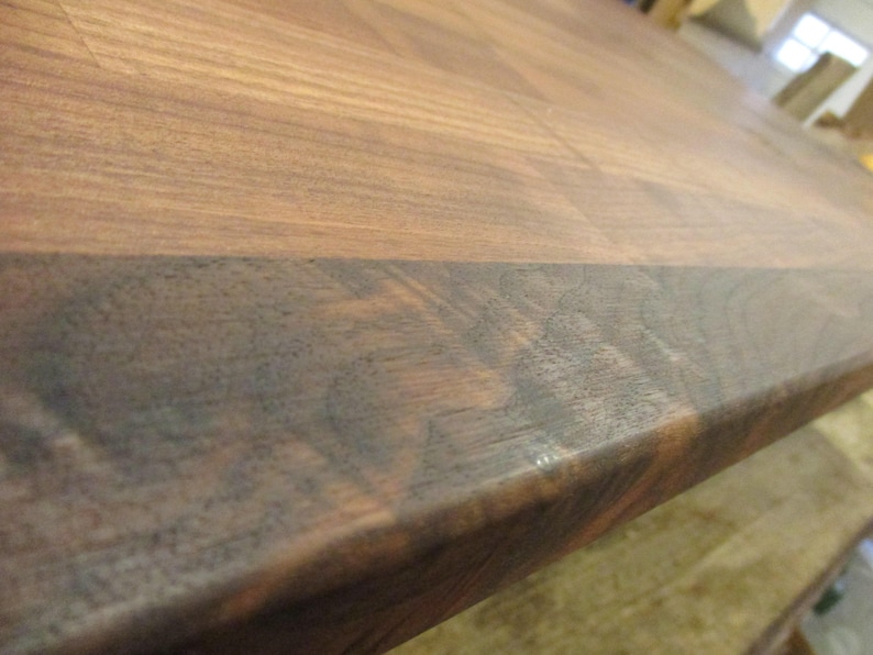 May include: Close-up of a dark brown wooden countertop with a lighter brown edge. The wood grain is visible and the surface is smooth.