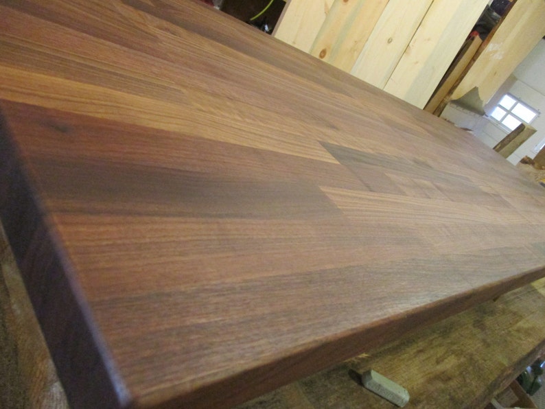 May include: A close-up of a dark brown wooden countertop made of walnut wood. The wood grain is visible and the surface is smooth.
