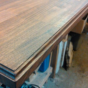 Pu&ograve; includere: Primo piano di un piano da tavolo in legno marrone scuro con un bordo decorativo. Il piano del tavolo &egrave; realizzato in assi di legno e ha una finitura liscia e lucida.