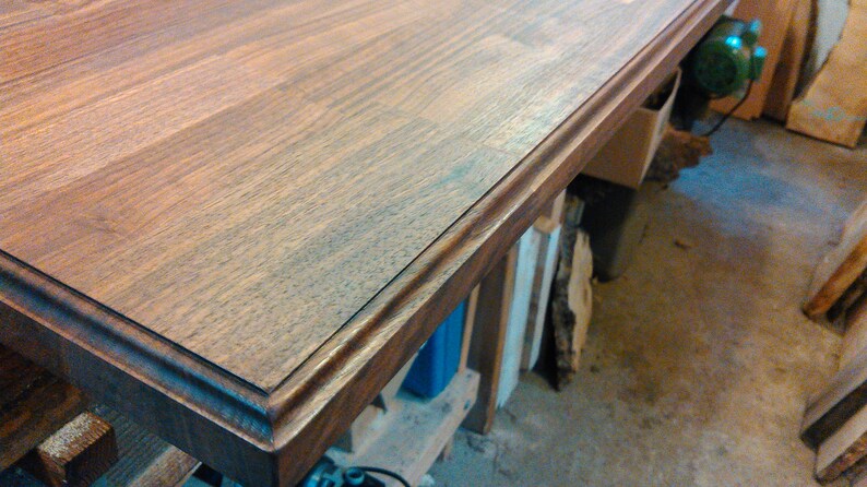 Pu&ograve; includere: Primo piano di un piano da tavolo in legno marrone scuro con un bordo decorativo. Il piano del tavolo &egrave; realizzato in assi di legno e ha una finitura liscia e lucida.