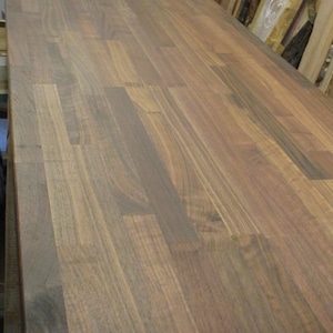 May include: A close-up of a dark brown wood countertop made of walnut planks. The wood has a natural grain pattern and a smooth finish.