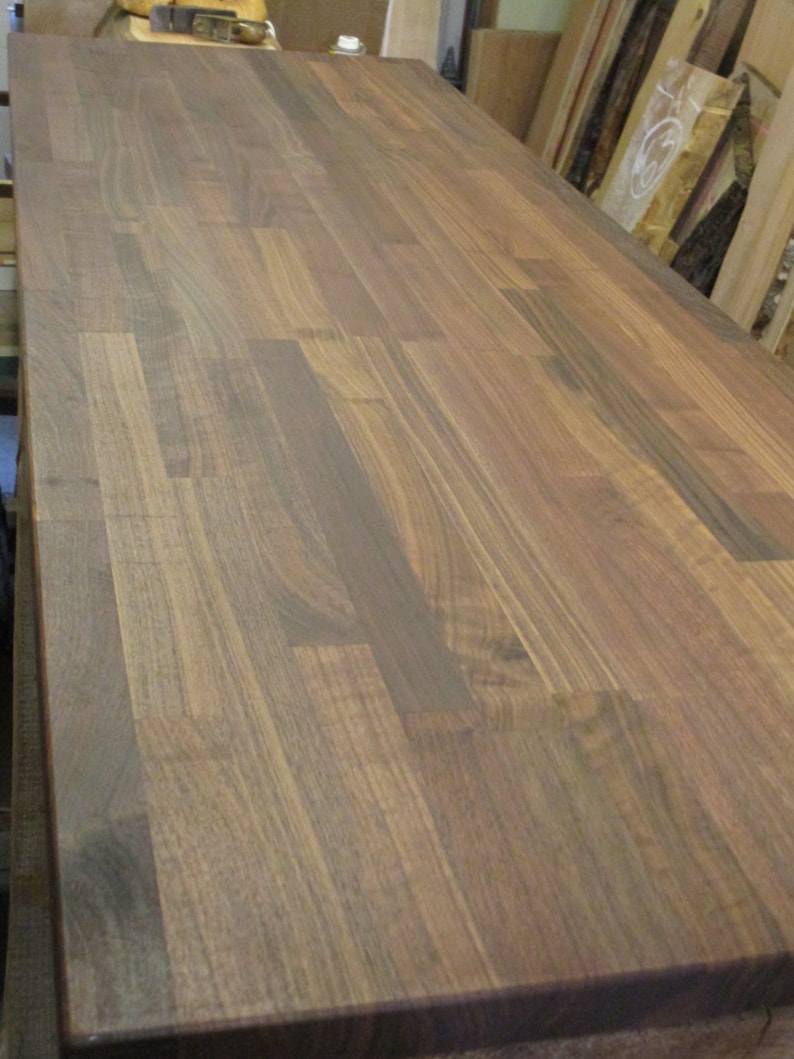 May include: A close-up of a dark brown wood countertop made of walnut planks. The wood has a natural grain pattern and a smooth finish.