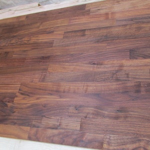 Pu&ograve; includere: Un primo piano di un piano di lavoro in legno marrone scuro realizzato con assi di noce. Il legno ha una venatura naturale e una finitura liscia.