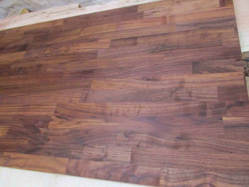 Pu&ograve; includere: Un primo piano di un piano di lavoro in legno marrone scuro realizzato con assi di noce. Il legno ha una venatura naturale e una finitura liscia.