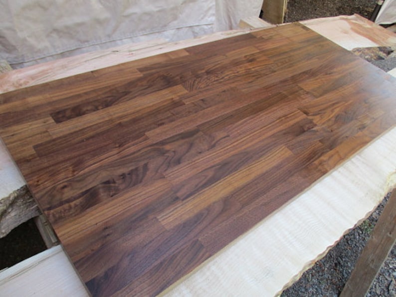 Pu&ograve; includere: Un primo piano di un piano di lavoro in legno marrone scuro realizzato con assi di noce. Il legno ha una venatura naturale ed &egrave; lucidato a una finitura liscia.
