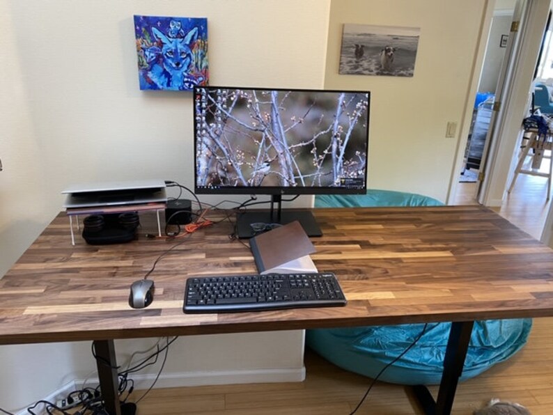 Pu&ograve; includere: Una scrivania in legno con una tastiera nera, un mouse per computer e un supporto per laptop. Un monitor con una scena naturale &egrave; sulla scrivania. Una poltrona a sacco turchese &egrave; sullo sfondo.