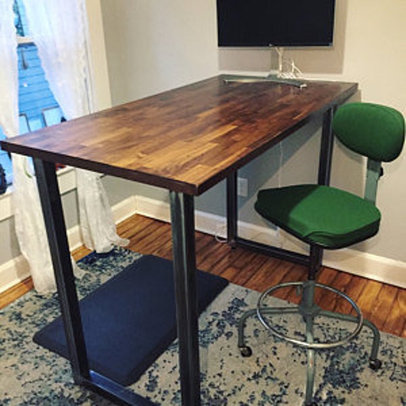 May include: A dark wood standing desk with a black metal frame and a green office chair. The desk is on a rug with a black mat underneath.