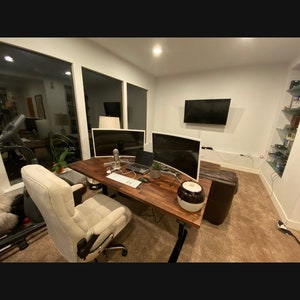 May include: A modern home office with a wooden desk, two curved computer monitors, a white office chair, and a brown leather couch. The desk has a laptop, a keyboard, a mouse, and a glass of water on it.