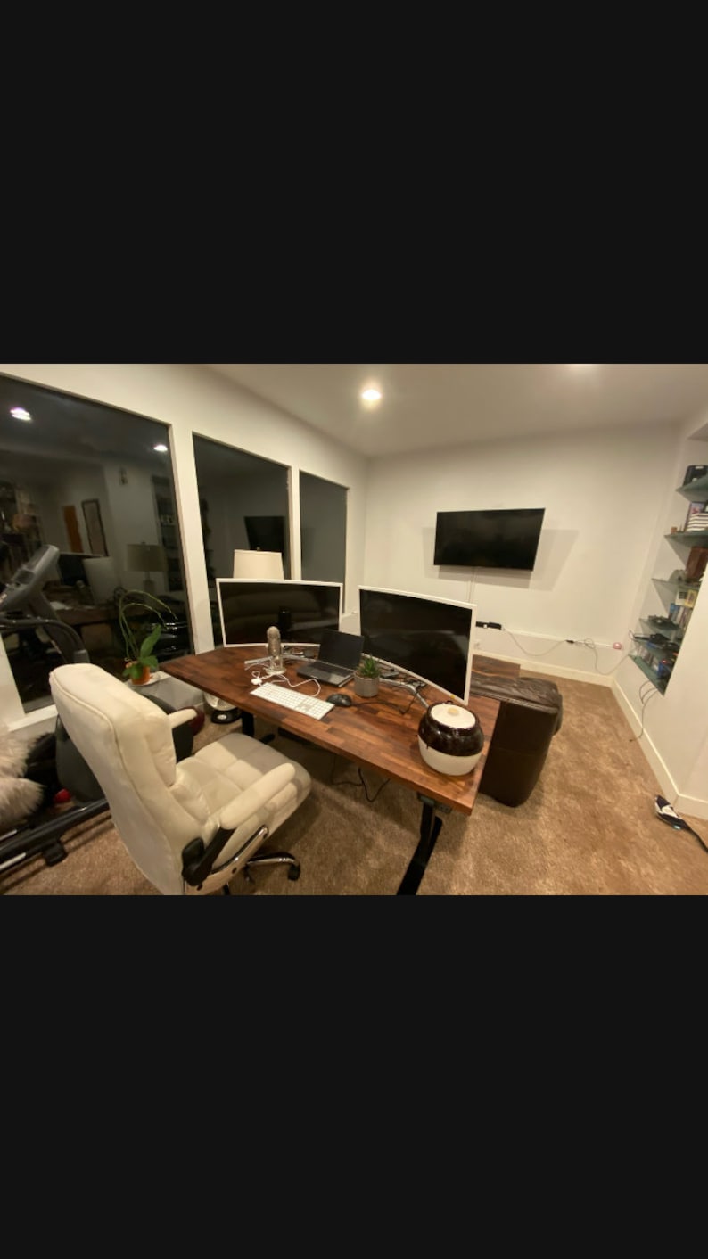 May include: A modern home office with a wooden desk, two curved computer monitors, a white office chair, and a brown leather couch. The desk has a laptop, a keyboard, a mouse, and a glass of water on it.