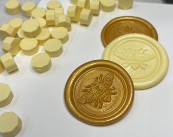 May include: Three wax seals with a bee design. Two are white with gold bees and one is gold with a white bee.