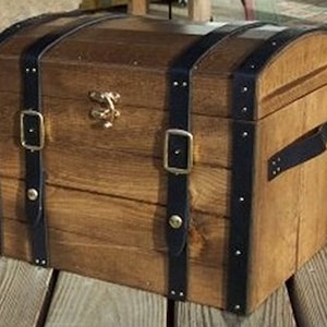 May include: A wooden chest with a curved top, featuring dark blue leather straps and metal buckles. The chest has a brass clasp and is made of light brown wood. The chest has a handle on the side.