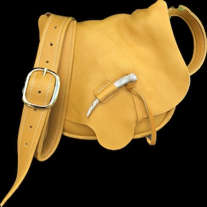 May include: A mustard yellow leather crossbody bag with a long strap and a decorative antler accent.