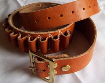 May include: A brown leather belt with a built-in cartridge holder. The belt has a brass buckle and is designed to hold shotgun shells.