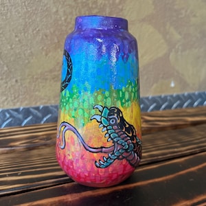 May include: A hand-painted wooden vase with a vibrant rainbow gradient. The vase features a detailed illustration of a creature with claws and tentacles. The design includes a black and white circular symbol. The vase is a unique piece of art.