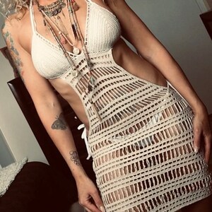 K&ouml;nnte beinhalten: Ein wei&szlig;es H&auml;kelkleid mit einem Halterneck und einem Ausschnitt. Das Kleid ist aus einem leichten, atmungsaktiven Stoff gefertigt und hat eine lockere Passform.