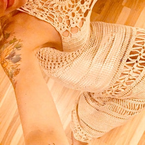 May include: A white crochet dress with a delicate floral pattern. The dress has a halter neckline and a flowing skirt.