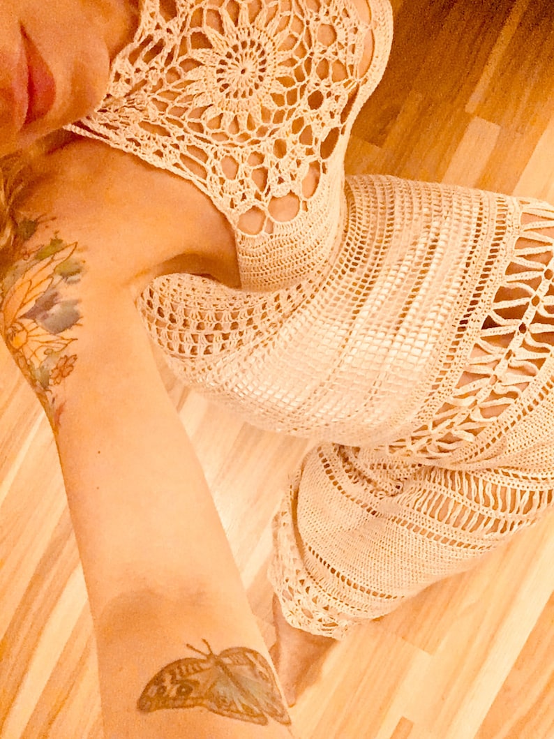 May include: A white crochet dress with a delicate floral pattern. The dress has a halter neckline and a flowing skirt.