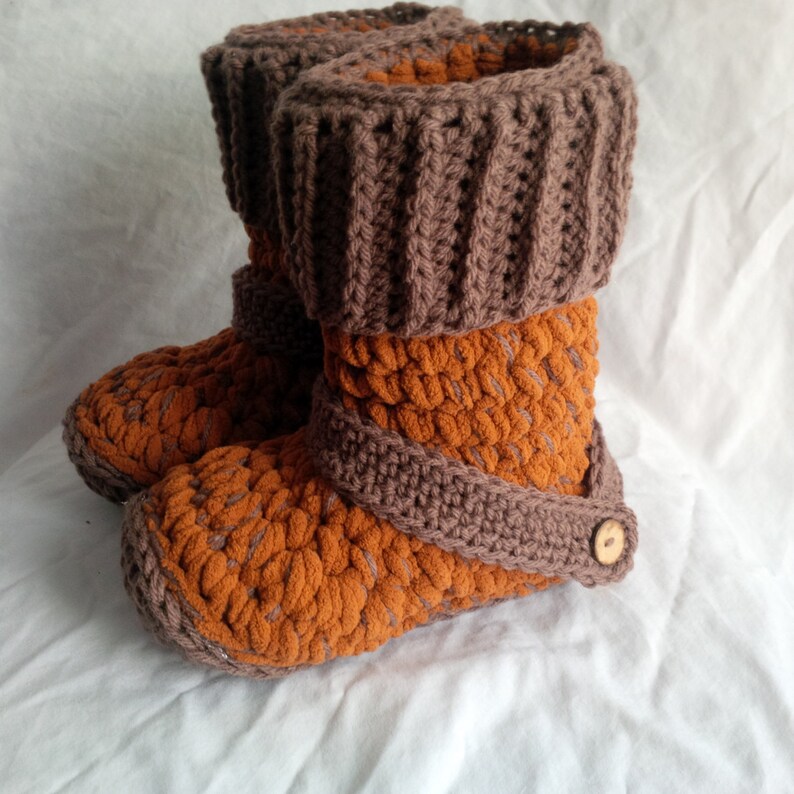 May include: A pair of brown and orange crocheted slippers with a brown crocheted cuff. The slippers have a button on the side.