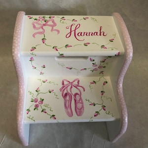 May include: White wooden step stool with pink polka dots and a hand-painted design. The top step features a pink bow and the name "Hannah". The bottom step has a pair of pink ballet shoes with a pink bow.