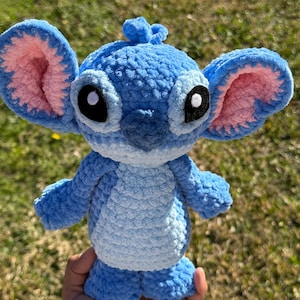 May include: A handmade blue crochet plush toy with large ears, black eyes, and a small tuft of hair. The plush has a light blue belly and pink inner ears. The toy is approximately 8 inches tall.