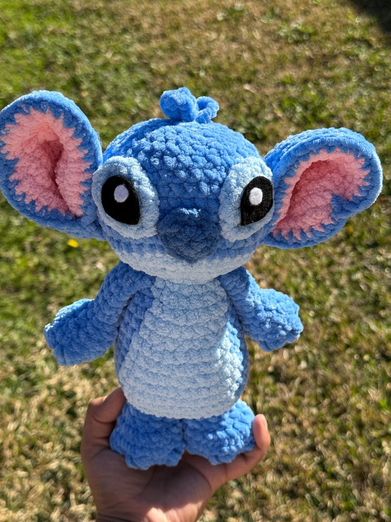 May include: A handmade blue crochet plush toy with large ears, black eyes, and a small tuft of hair. The plush has a light blue belly and pink inner ears. The toy is approximately 8 inches tall.
