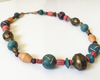 May include: A colorful beaded necklace with teal, pink, brown, and purple beads. The necklace has metal accents and a bell charm.