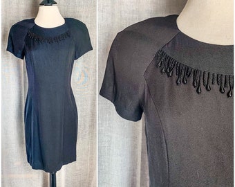 May include: A black short-sleeved dress with a beaded neckline. The beads are black and have a teardrop shape.