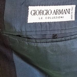 May include: A close-up of a dark blue fabric with a white label that reads "Giorgio Armani Le Collezioni Made in Italy".