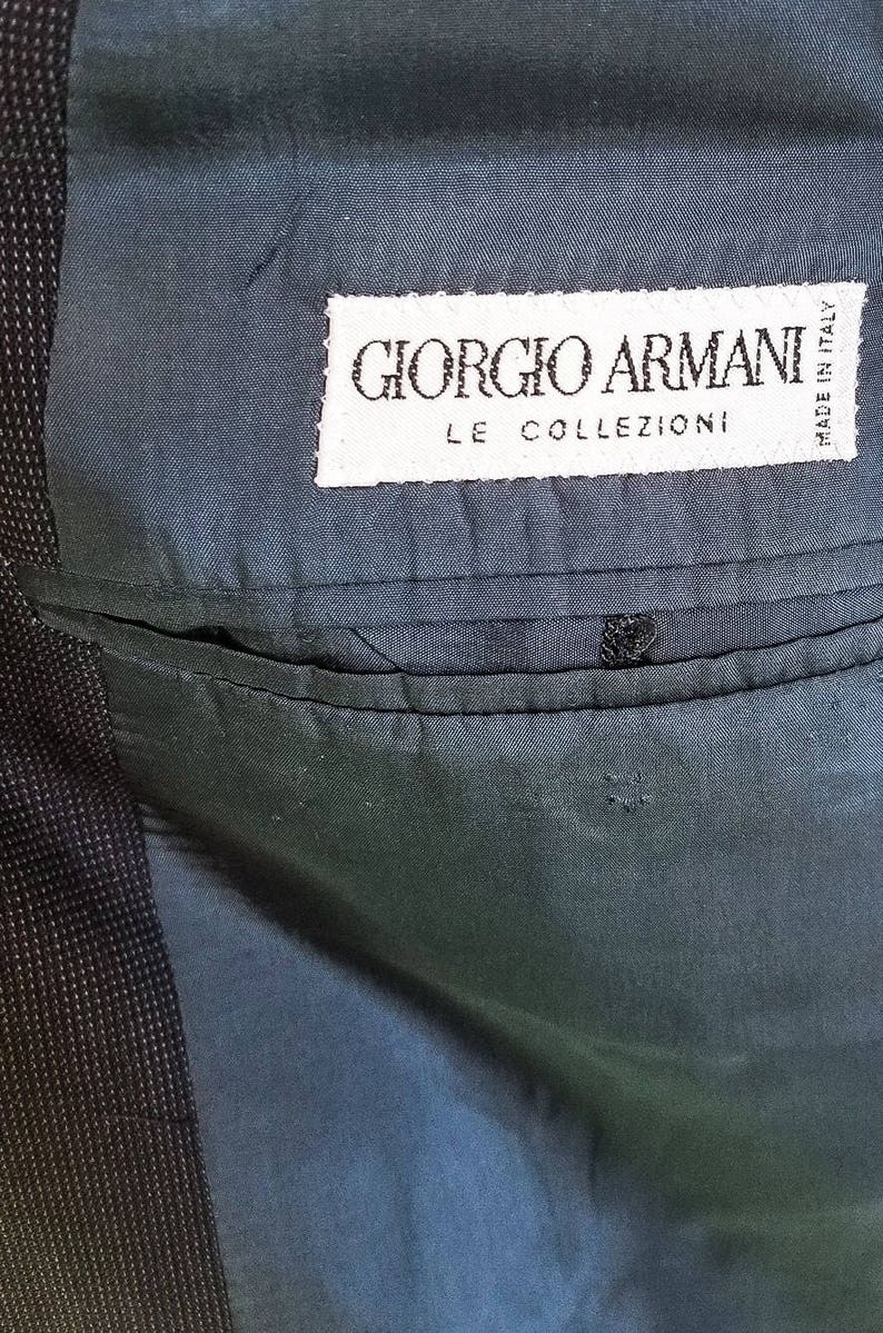May include: A close-up of a dark blue fabric with a white label that reads "Giorgio Armani Le Collezioni Made in Italy".