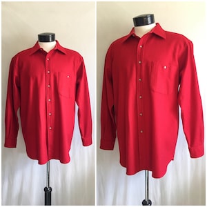 Puede incluir: Una camisa roja de manga larga con botones y un bolsillo único en el pecho. La camisa tiene botones plateados y está hecha de una tela suave y texturizada.