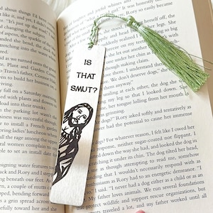 May include: A wooden bookmark with a green tassel. The bookmark features a black and white illustration of a man with a beard and the text "Is That Smut?" printed on it.