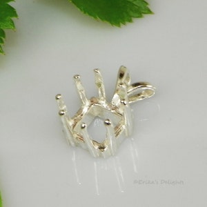 May include: A silver-colored pendant setting with prongs designed to hold a gemstone. The setting has an open, geometric design with a loop for a chain. The pendant is shown on a white surface.