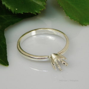 May include: A silver ring setting with a six-prong design. The ring is made of sterling silver and is ready to be set with a gemstone.