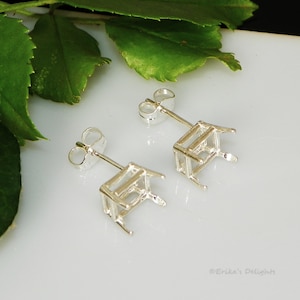 May include: A pair of silver earring settings with a square bezel for a gemstone. The settings are designed to be used with a post and back.