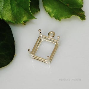 May include: A silver-colored rectangular pendant setting with four prongs at the corners and a loop at the top for a chain. The setting is designed to hold a gemstone or other decorative element. The setting is shown against a white background.