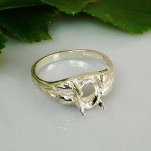 May include: Silver ring setting with an oval shaped center stone. The ring has a decorative design on the band.